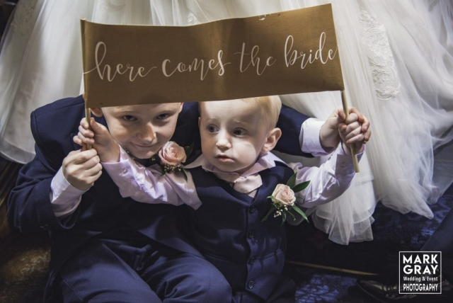 Page boys with here comes the bride sign
